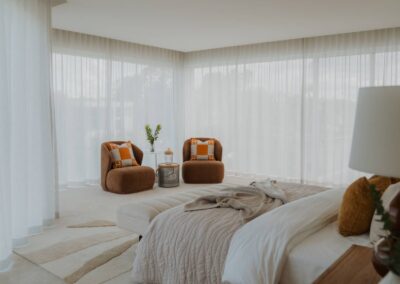 Two vibrant occasional chairs styled in a master bedroom with sheer curtains behind